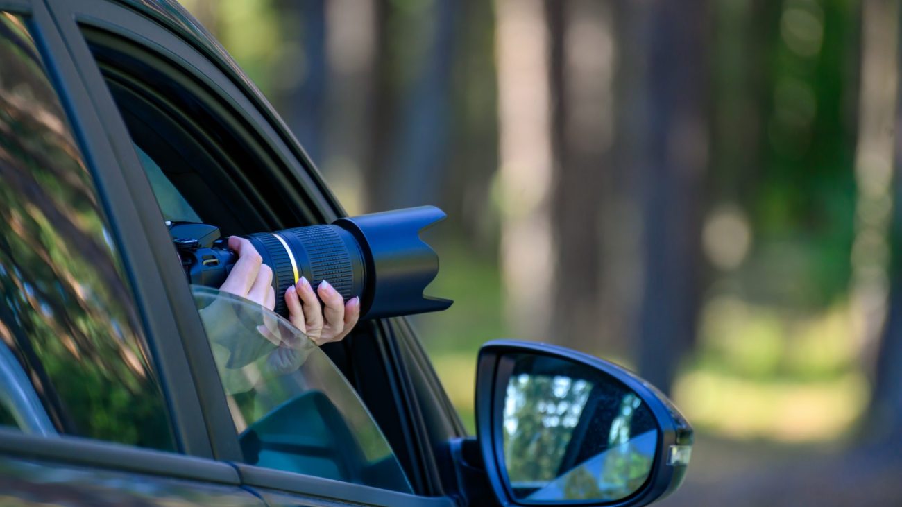 A private detective is sitting in the car, filming. The paparazzi sits in the car and photographs a famous person. Spy with a camera in the car.